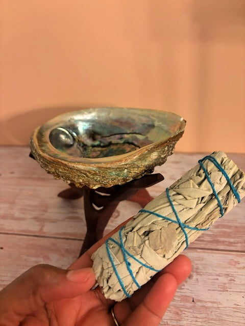 Hand holding a bundle of sage wrapped with blue twine in front of a ceramic bowl on a wooden surface.